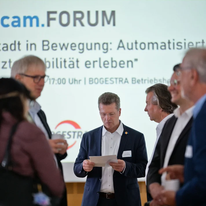 Gruppe von Personen in Businesskleidung vor einer Präsentationswand mit dem Schriftzug 'innocam.FORUM' und dem Thema 'Die Stadt in Bewegung Automatisierte und vernetzte Mobilität erleben'