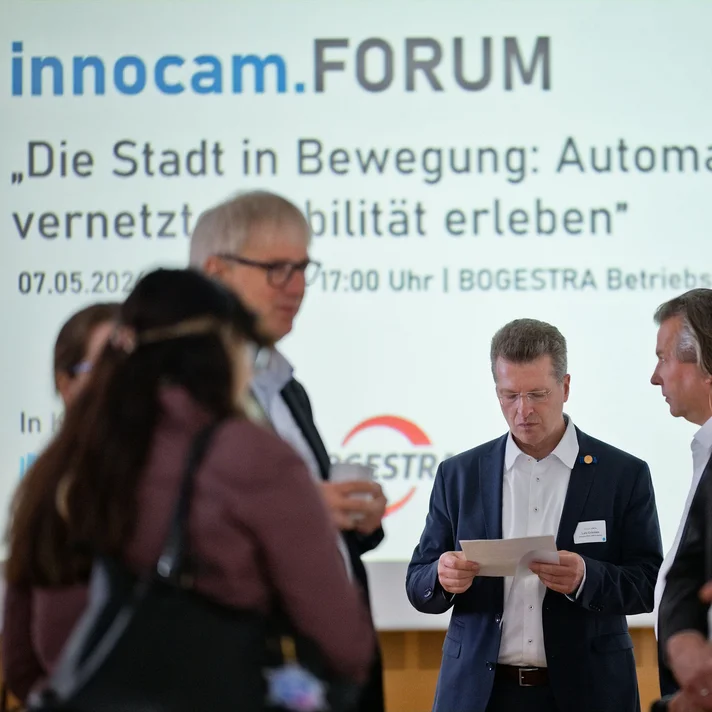 Gruppe von Personen in Businesskleidung vor einer Präsentationswand mit dem Schriftzug 'innocam.FORUM' und dem Thema 'Die Stadt in Bewegung Automatisierte und vernetzte Mobilität erleben'