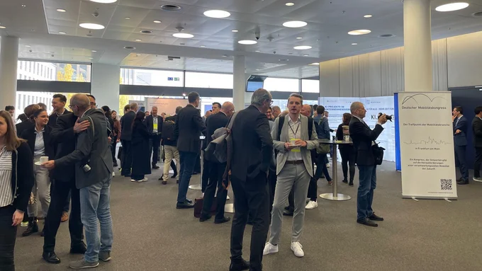 Mehrere Personen in Businesskleidung stehen und unterhalten sich in einem hellen, modernen Konferenzraum beim Mobilitätskongress.
