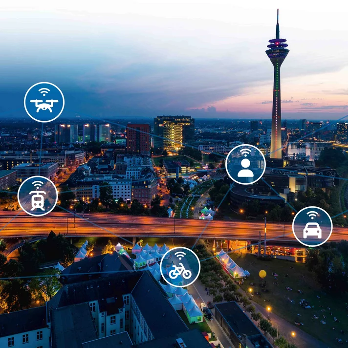 Blick über eine abendliche Stadt mit vernetztem Verkehrsnetz und Symbolen für verschiedene Mobilitätsformen wie Auto, Zug, Flugzeug und Fahrrad.