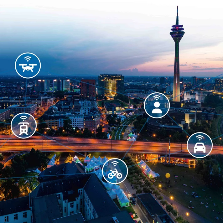 Blick über eine abendliche Stadt mit vernetztem Verkehrsnetz und Symbolen für verschiedene Mobilitätsformen wie Auto, Zug, Flugzeug und Fahrrad.