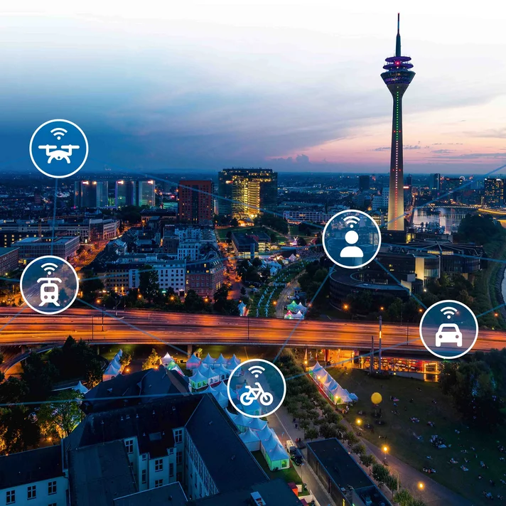 Blick über eine abendliche Stadt mit vernetztem Verkehrsnetz und Symbolen für verschiedene Mobilitätsformen wie Auto, Zug, Flugzeug und Fahrrad.