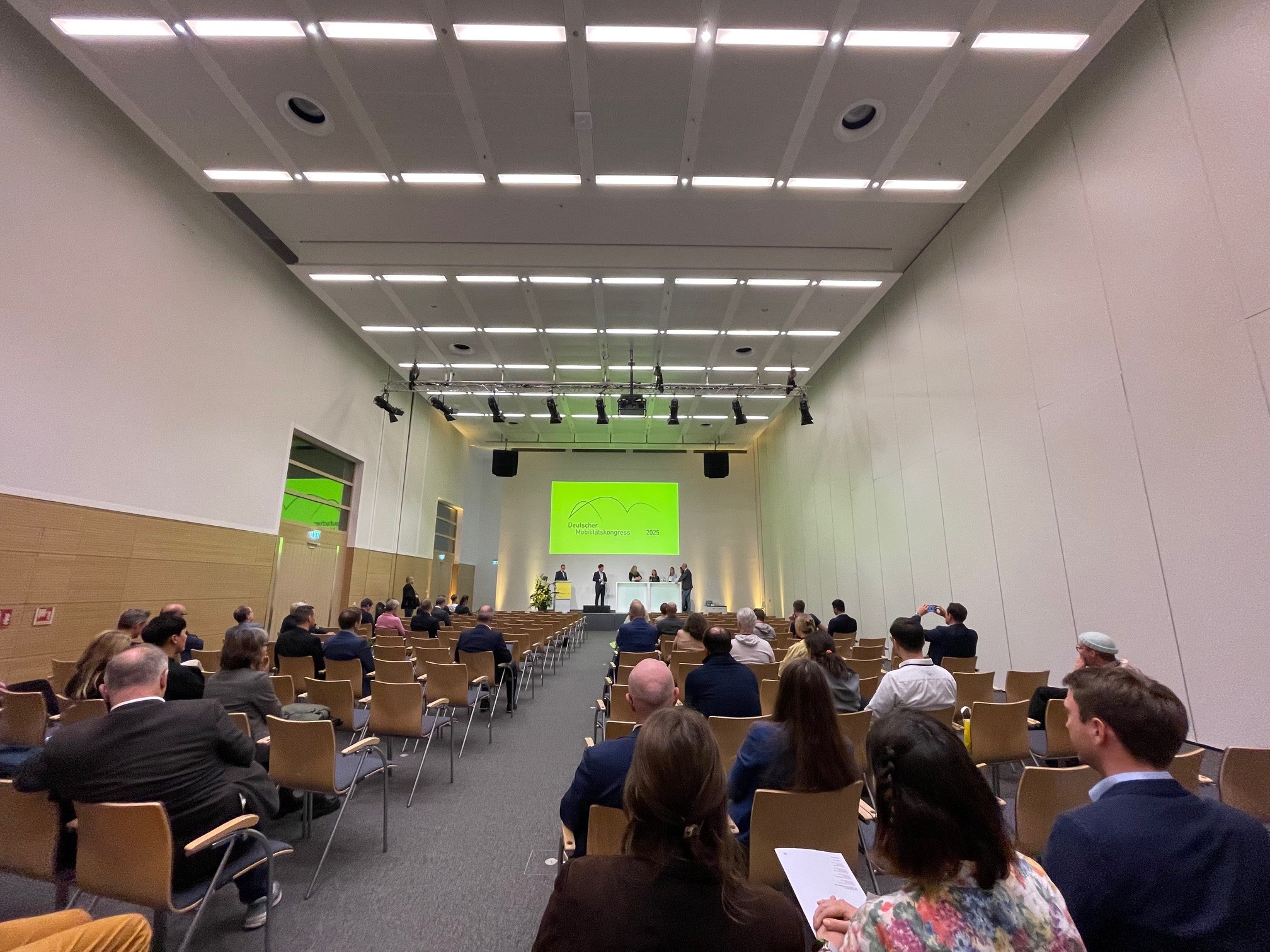 Konferenzraum mit Publikum und Podium, auf dem mehrere Personen bei einem Mobilitätskongress sprechen.