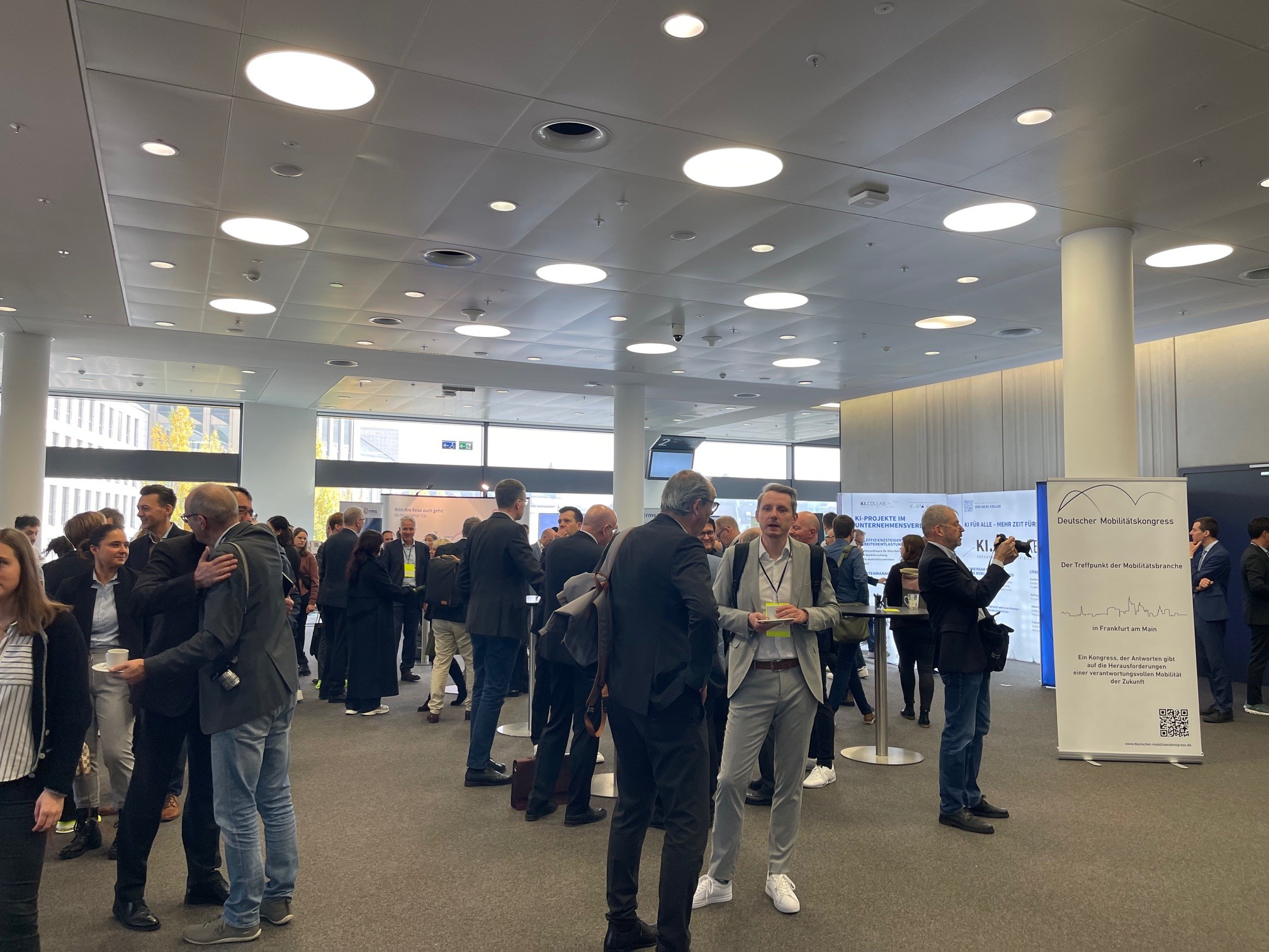 Mehrere Personen in Businesskleidung stehen und unterhalten sich in einem hellen, modernen Konferenzraum beim Mobilitätskongress.