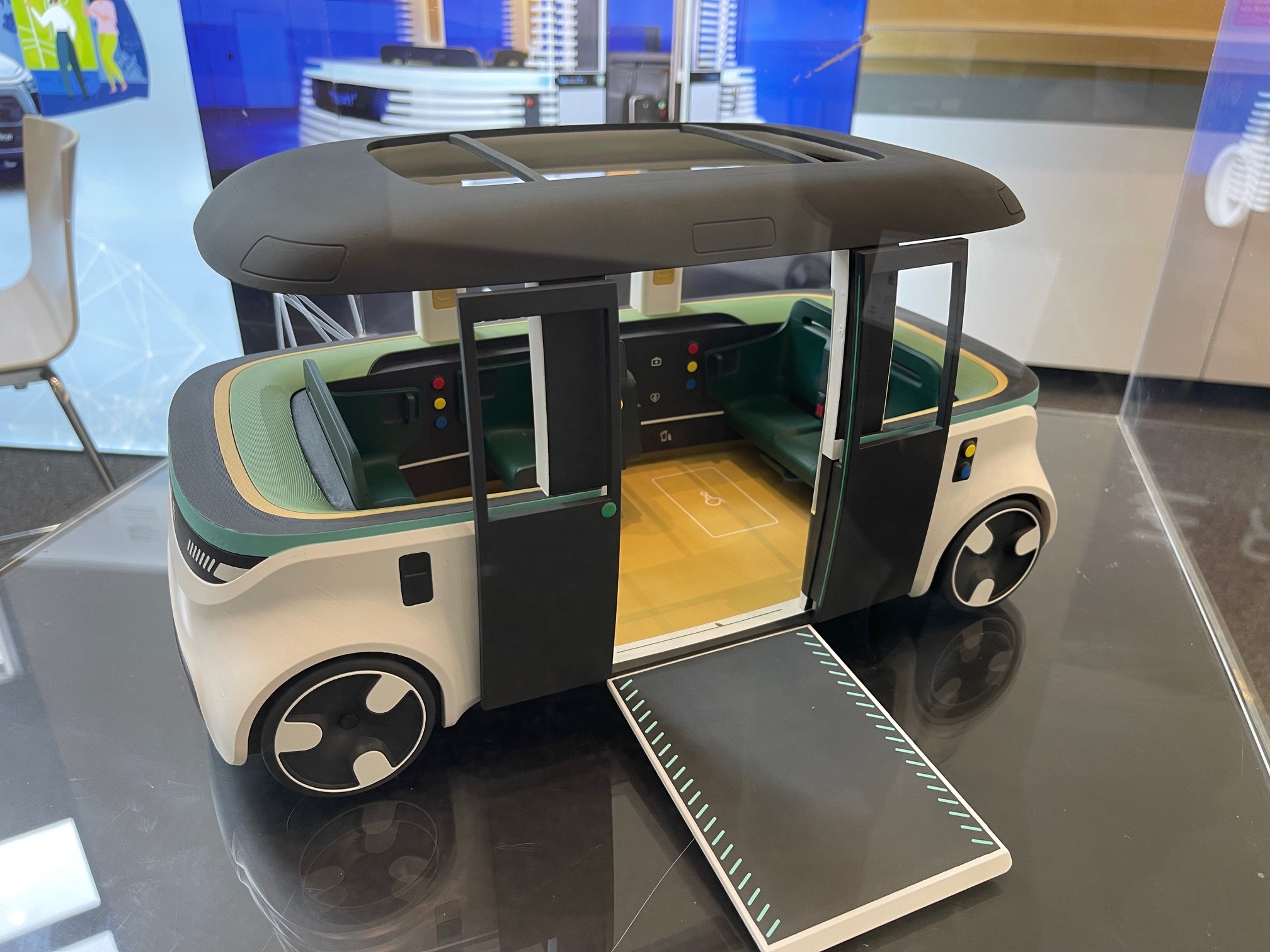 Modell eines autonomen, rechteckigen Fahrzeugs mit Schiebetüren und ausklappbarer Rampe, präsentiert auf einem Tisch beim Mobilitätskongress.