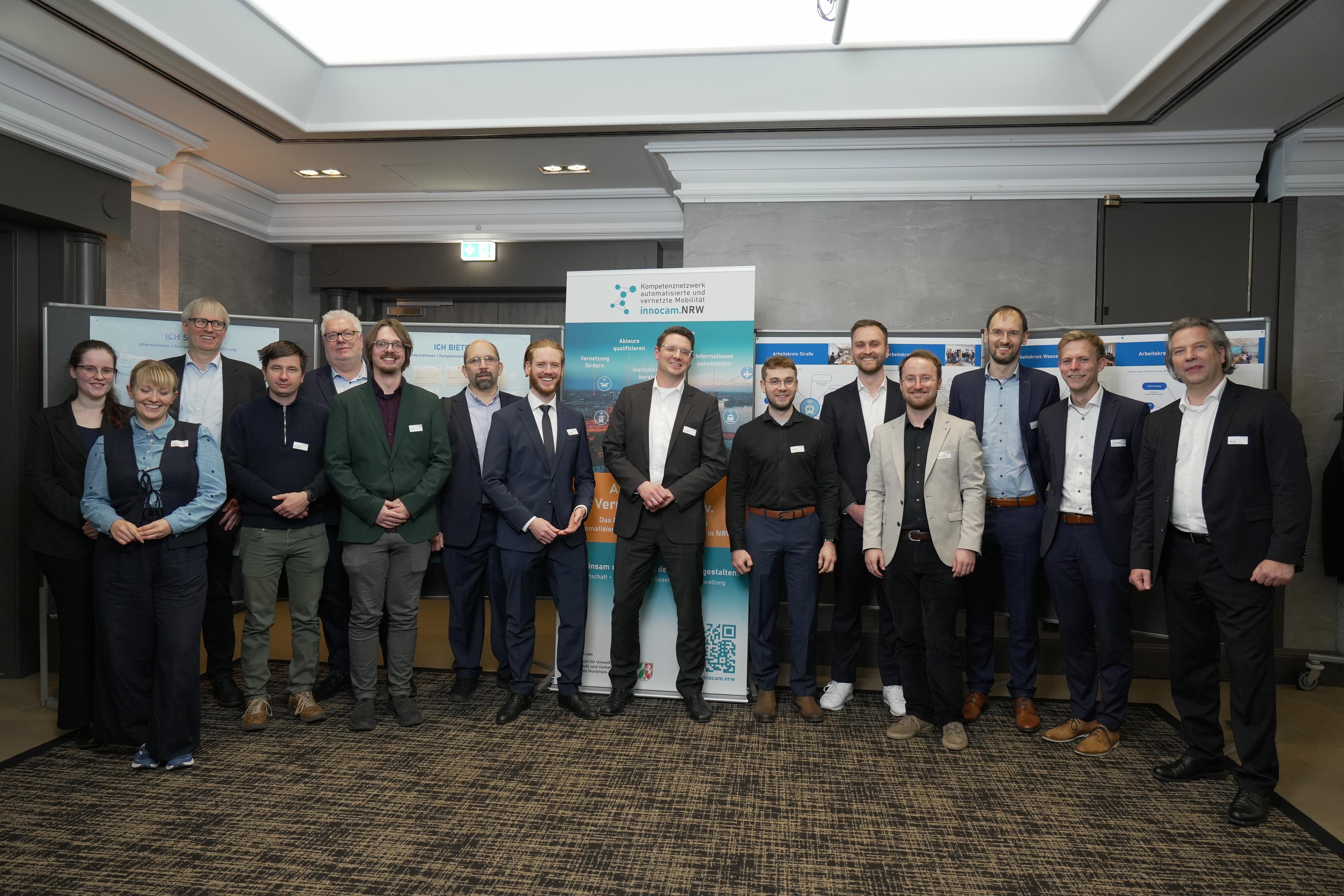 Gruppefoto von Personen in Business-Kleidung steht vor Bannern mit Logos und Texten zum innocam.NRW Mobility Meeting in einem Konferenzraum.