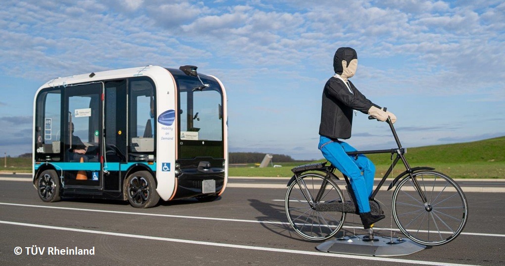 Fahrradfahrer-Dummy vor einem autonomen Shuttlebus auf einem Testgelände.